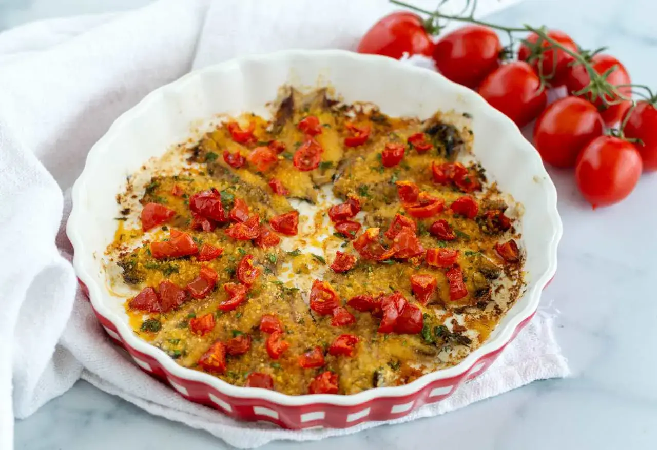 Piatto di alici al forno con pomodorini e pangrattato, pronto per essere gustato.
