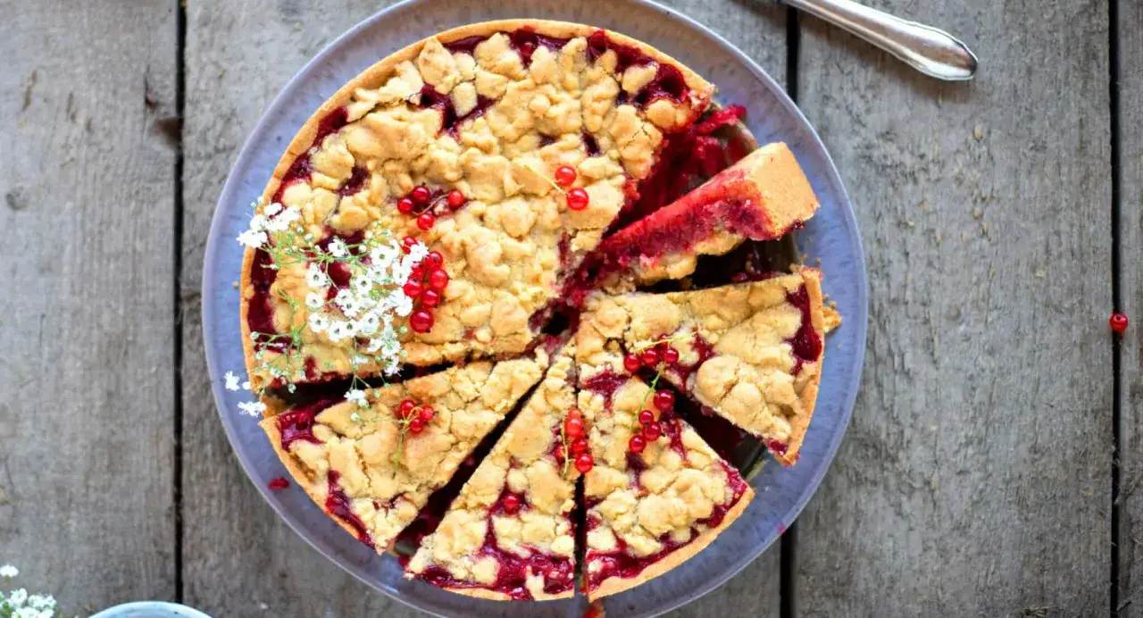 Saftiger Johannisbeer Kuchen mit Streuseln und frischen roten Johannisbeeren, garniert mit zarten weißen Blüten. Ein Genuss für Augen und Gaumen.