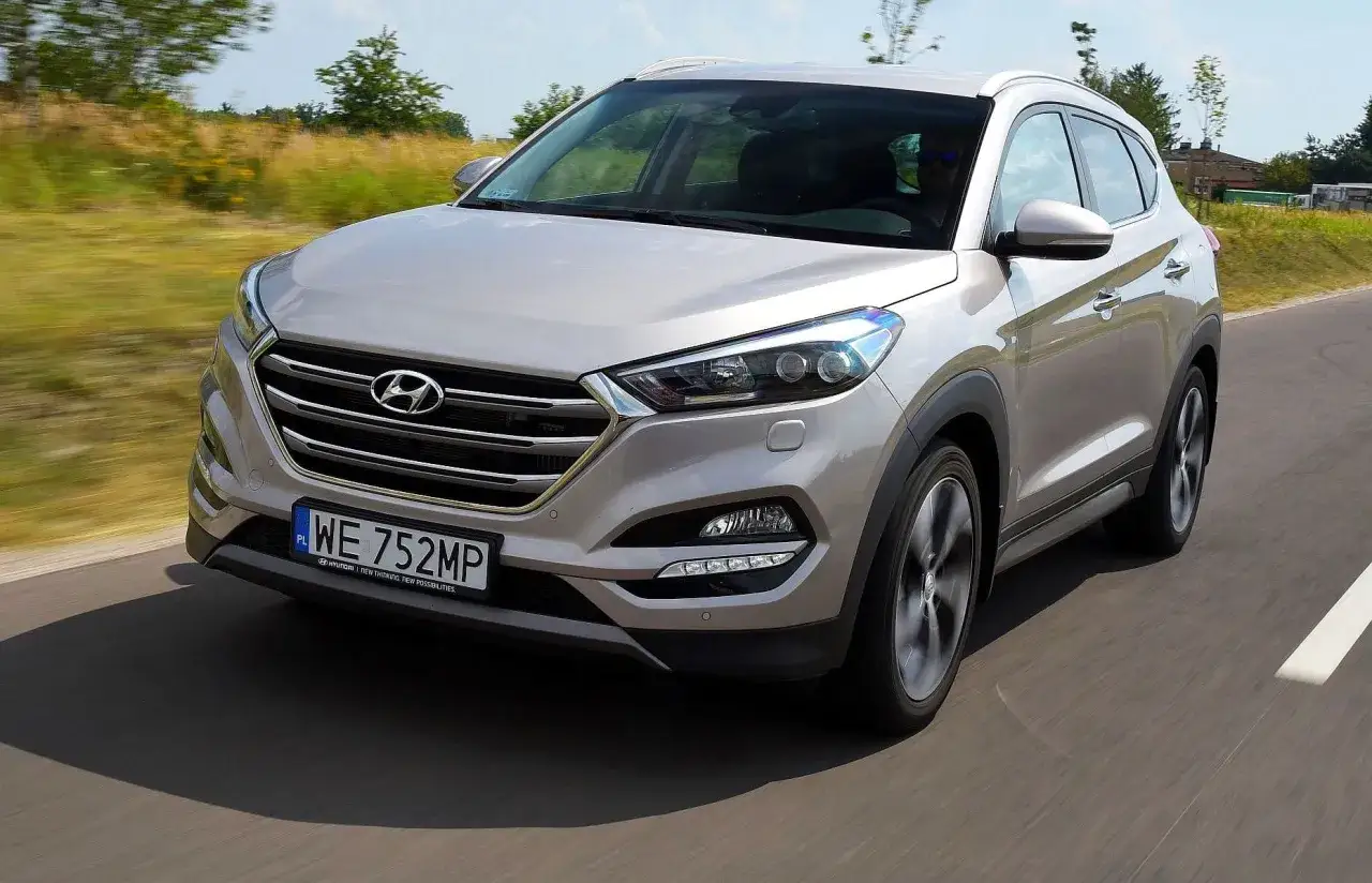 Srebrny Hyundai Tucson 3 jedzie po drodze, otoczony zielenią.