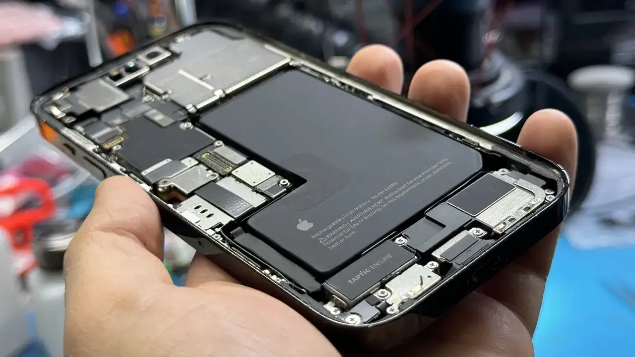 Rozłożony iPhone, widoczne wnętrze z baterią i podzespołami. Wygląda na to, że ten zalany iPhone wymaga naprawy.