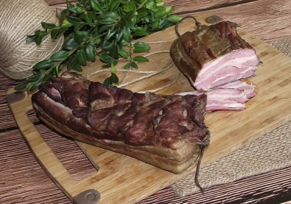 Dwa kawałki wędzonego boczku na desce. Jeden cały, drugi pokrojony w plastry. Zastanawiasz się, jak długo wędzić boczek?