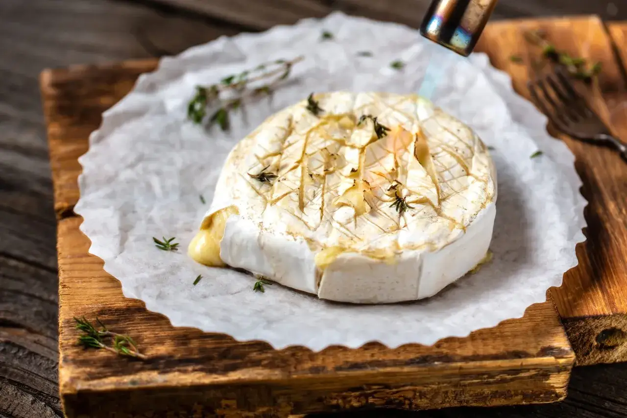 Ser camembert w ciąży, zapiekany palnikiem, z ziołami na desce.