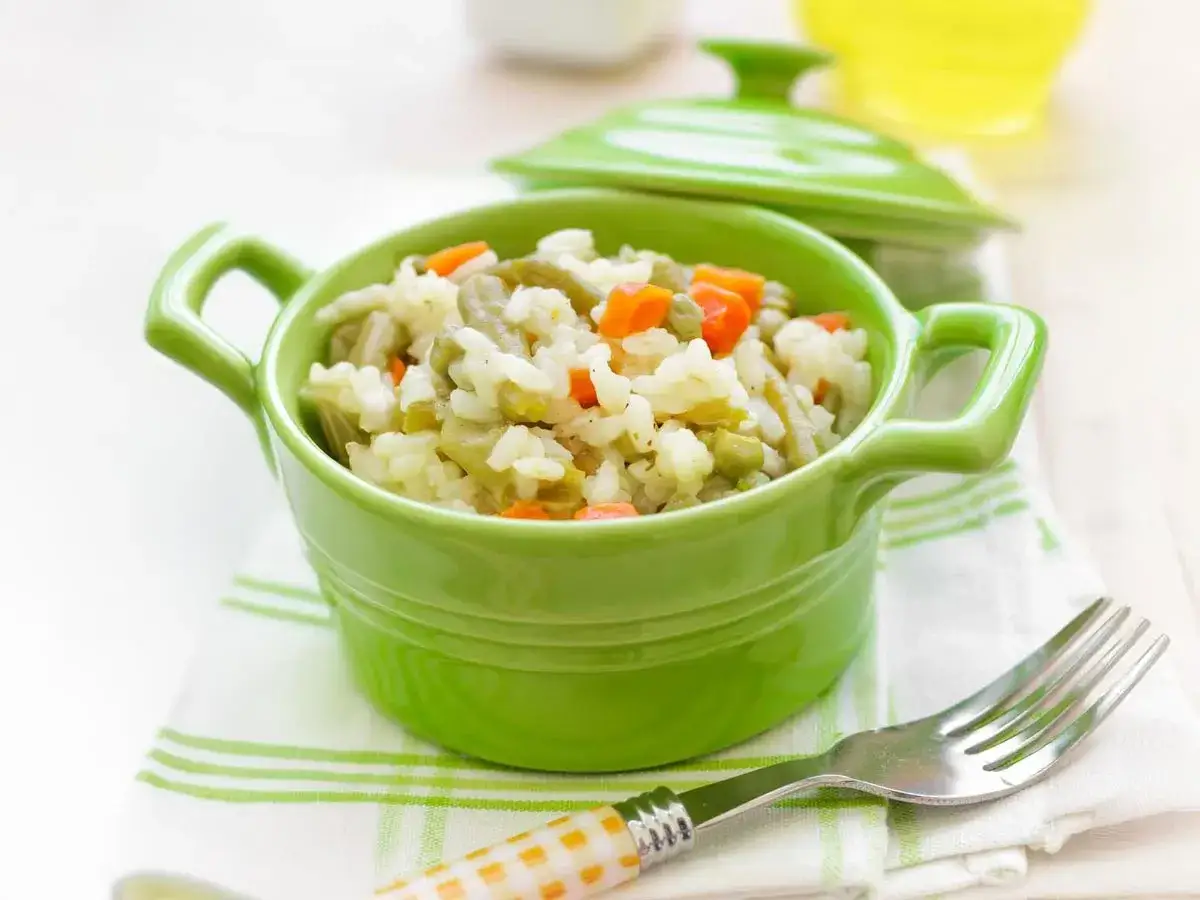 Arroz con verduras para bebé en un cuenco verde. Zanahoria, guisantes y judías verdes mezclados con arroz.