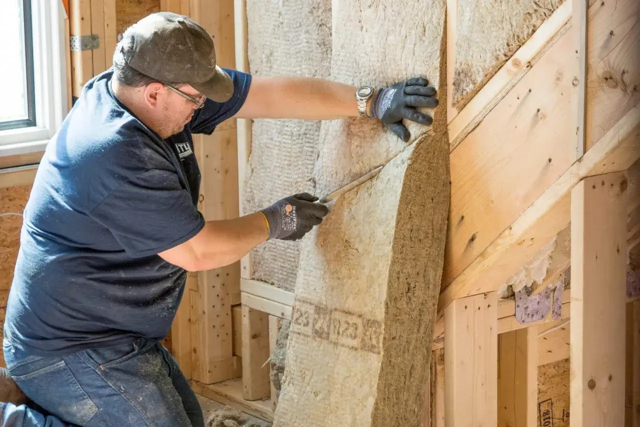 Un ouvrier ajuste un panneau isolant pour l'isolation par l'extérieur d'une maison en construction.
