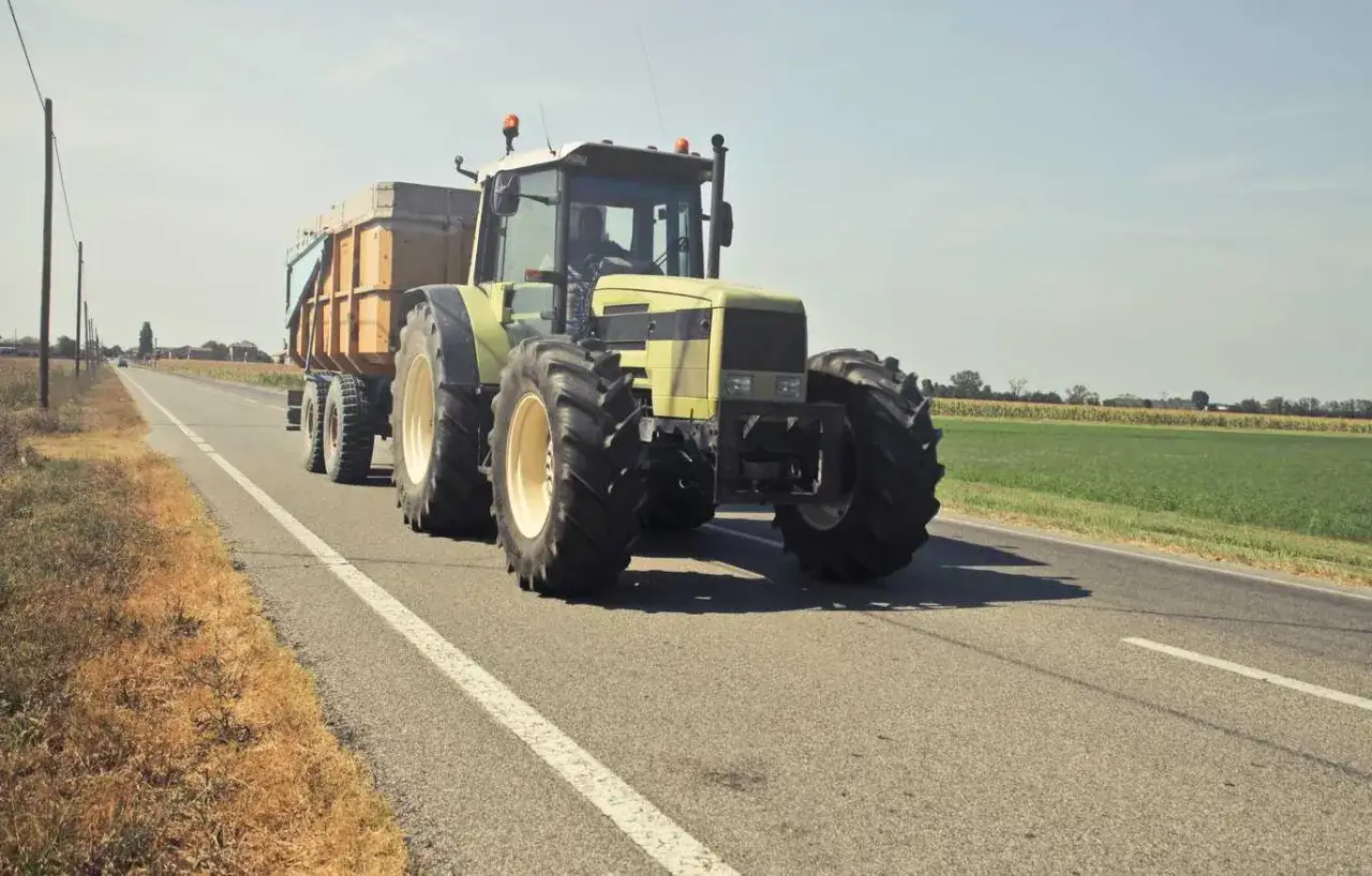 Żółty traktor z przyczepą jedzie drogą. Czy to najlepsza marka ciągnika?
