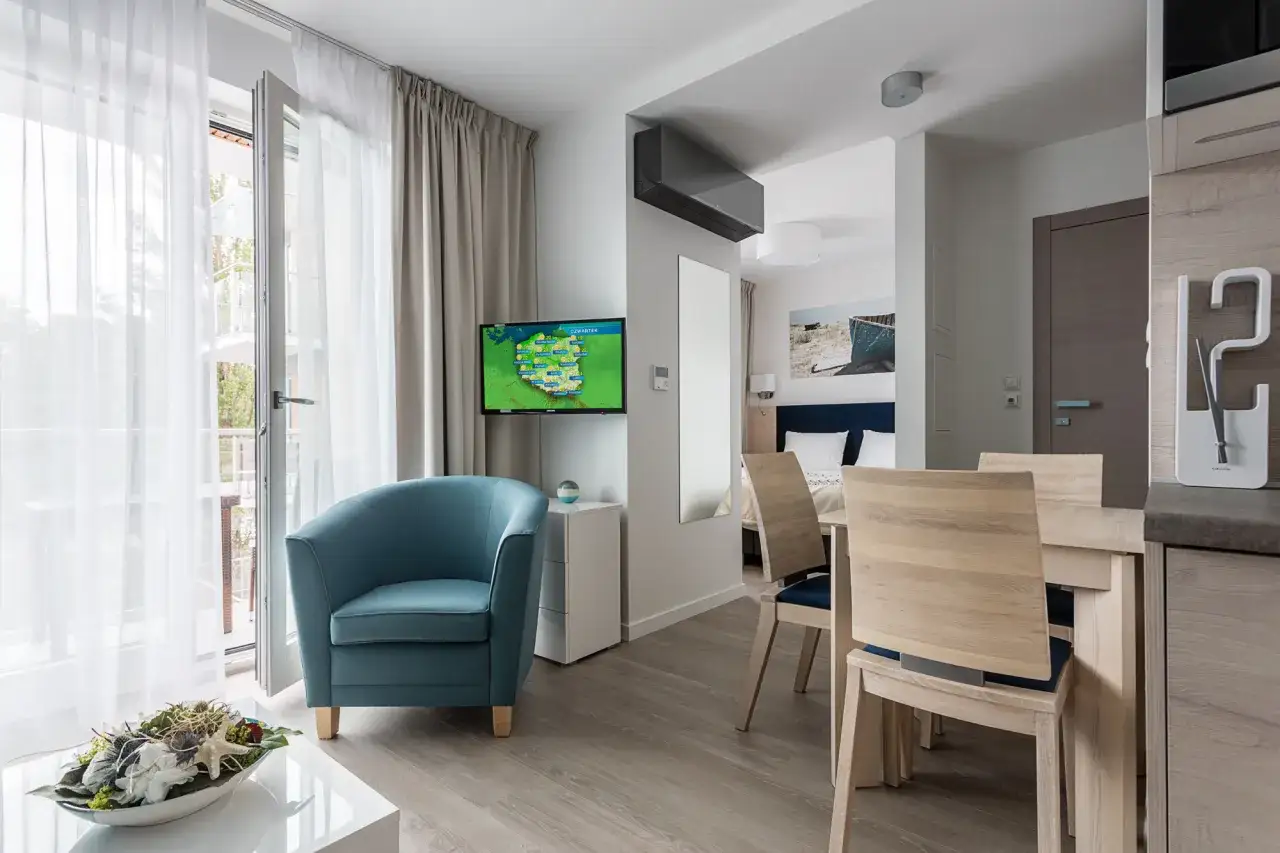 Nowoczesne apartamenty przy morzu. Wygodny fotel, stół z krzesłami i widok na balkon.