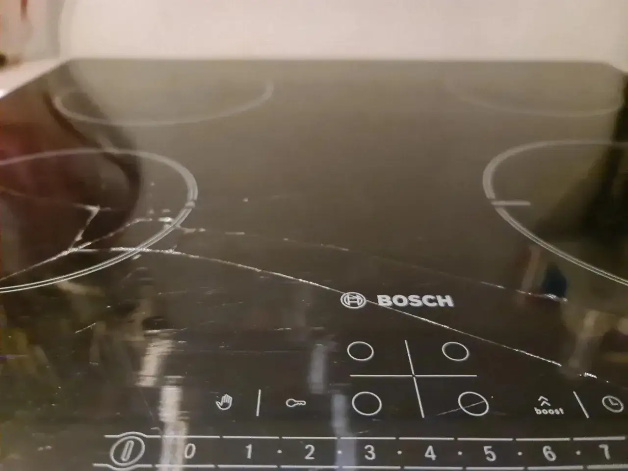 Pęknięta płyta indukcyjna Bosch z widocznymi zarysowaniami i pęknięciami na szkle.