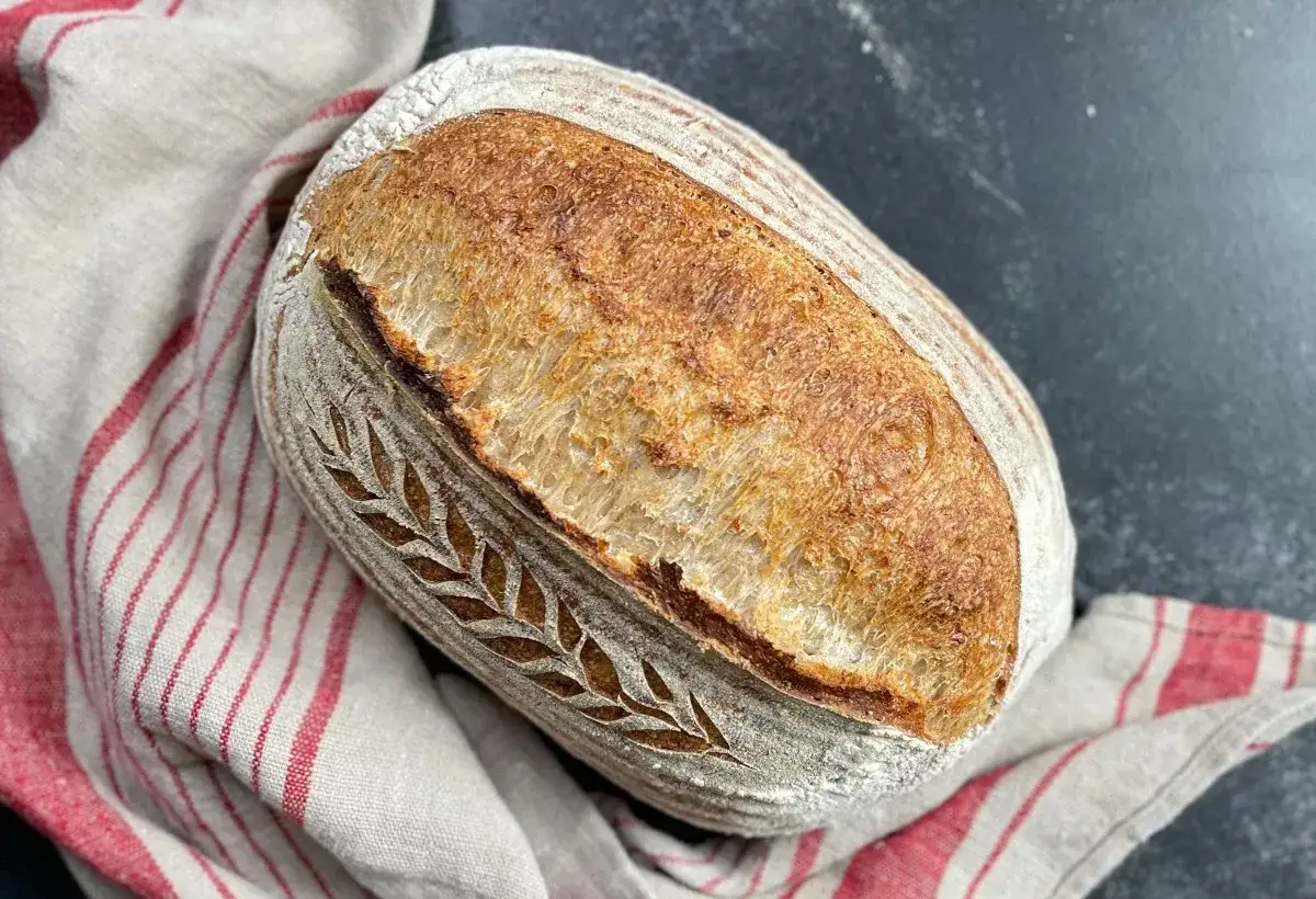 Pan de masa madre artesanal con corteza dorada y diseño de espiga, sobre un paño a rayas rojas.