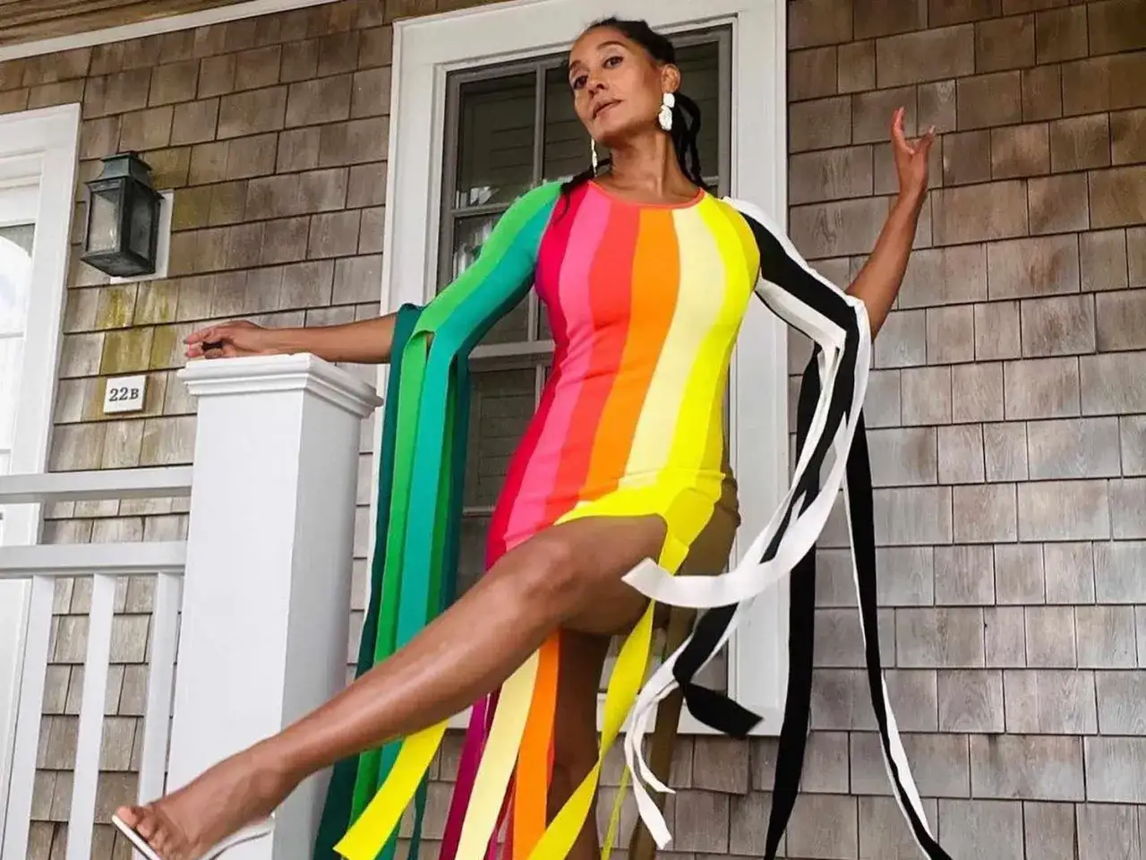Une femme pose sur un porche, vêtue d'une robe audacieuse en **color blocking** arc-en-ciel avec des manches originales.