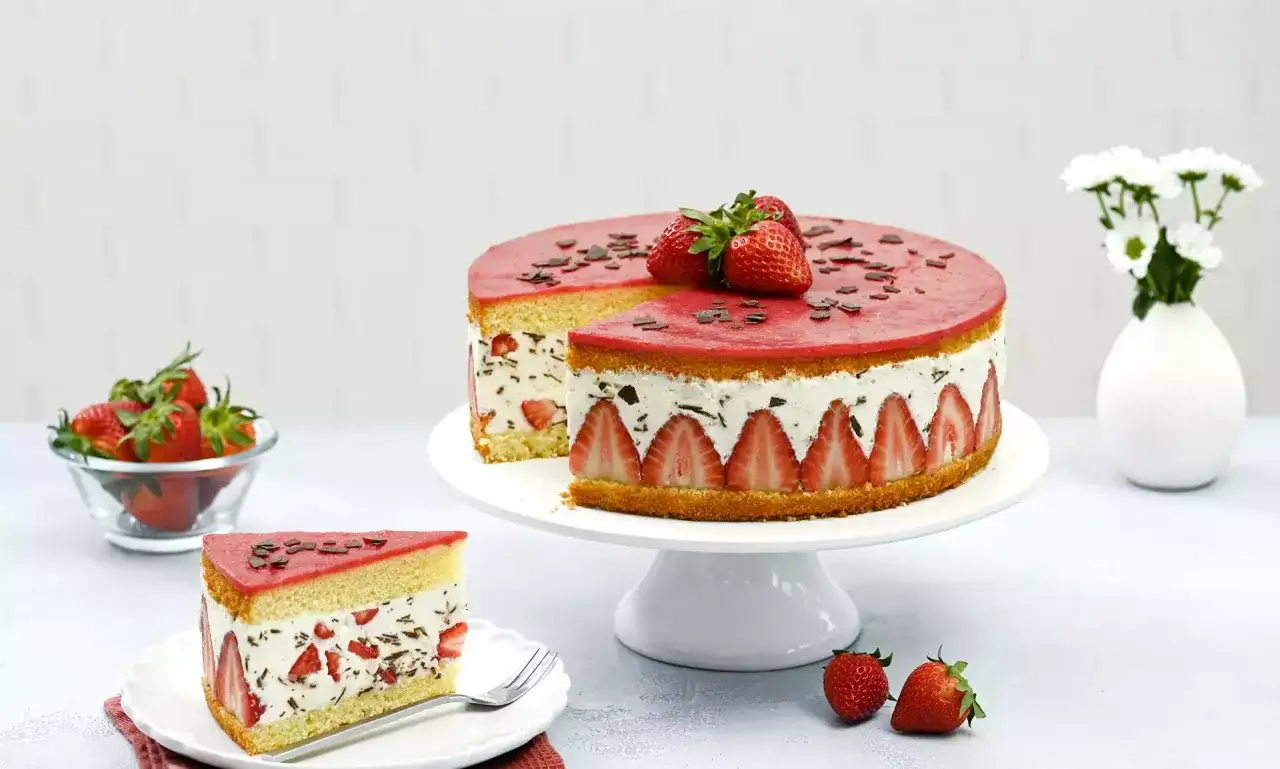 Eine köstliche Erdbeer Stracciatella Torte mit frischen Erdbeeren und Schokoladenstückchen, auf einem Tortenständer präsentiert.