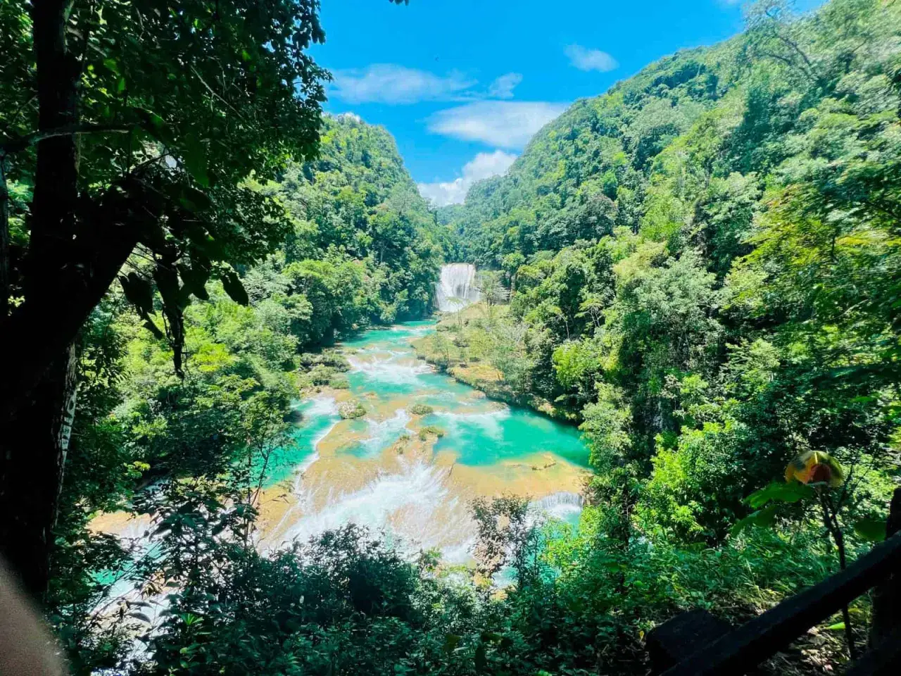 Cascada turquesa en la **selva** de **México**, rodeada de exuberante vegetación y montañas verdes.