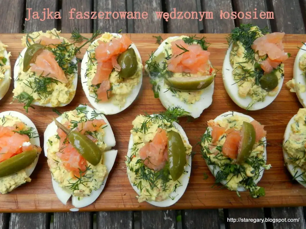 Jaja faszerowane wędzonym łososiem, ozdobione koperkiem i ogórkiem konserwowym, prezentują się apetycznie na desce.