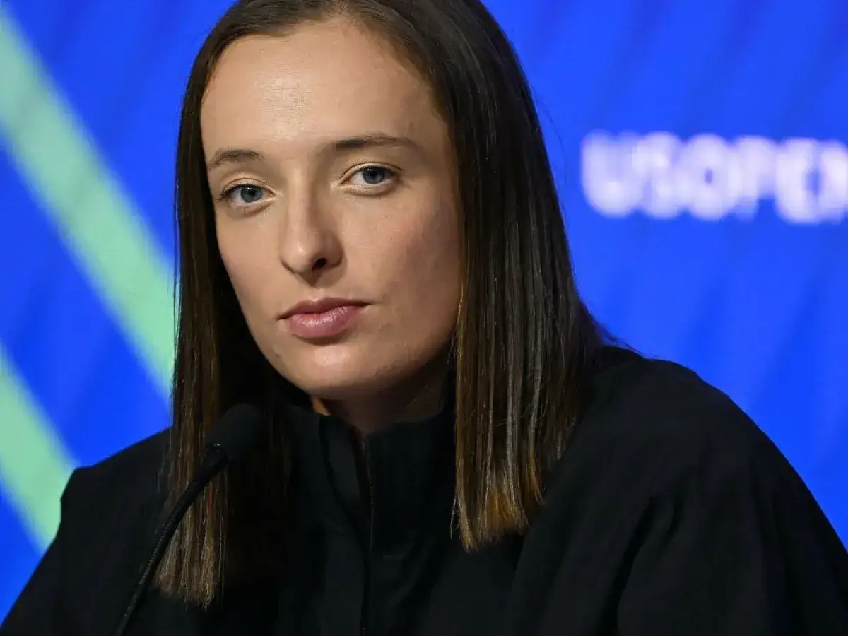 Iga Świątek, zamyślona, przed mikrofonem na tle niebieskiej ścianki z napisem US OPEN.