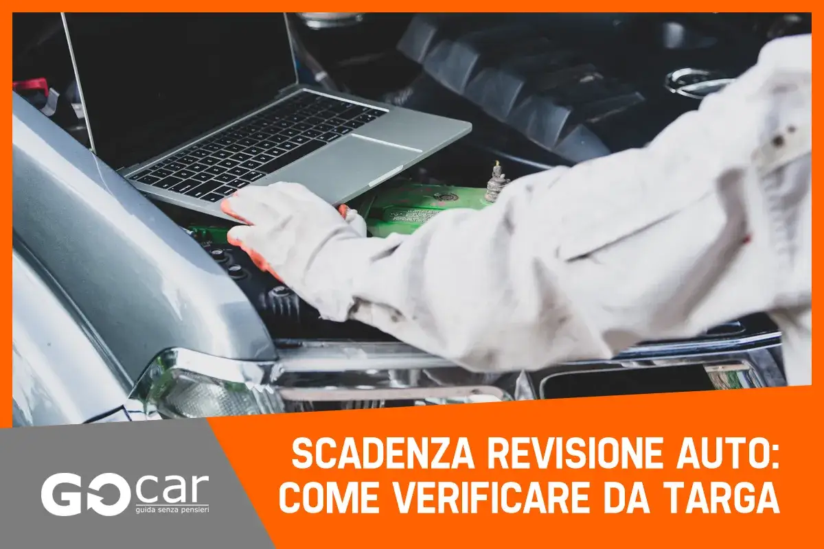 Meccanico con guanti controlla dati al computer per revisione auto reimmatricolata.