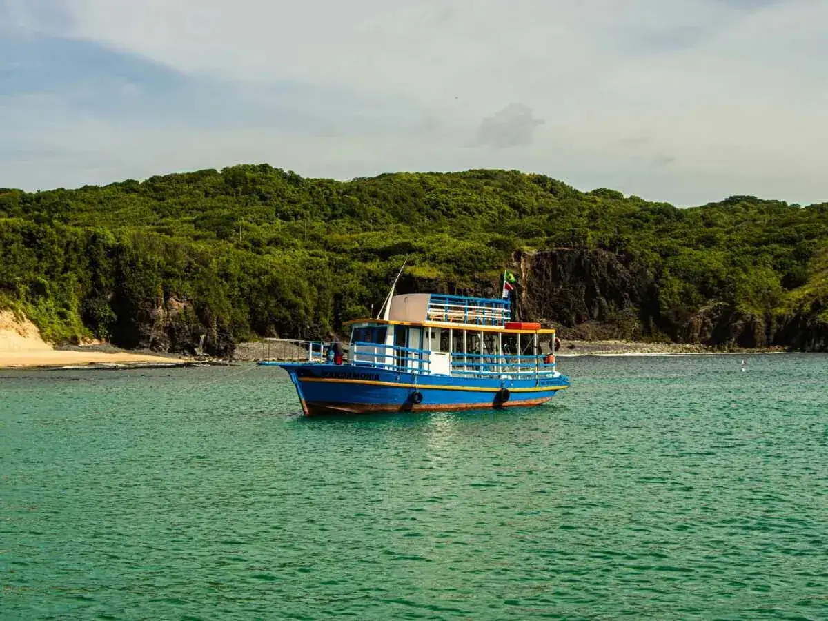 Bateau bleu ancré dans une eau turquoise, face à une île verdoyante. Idéal pour estimer le prix peinture bateau au m2.
