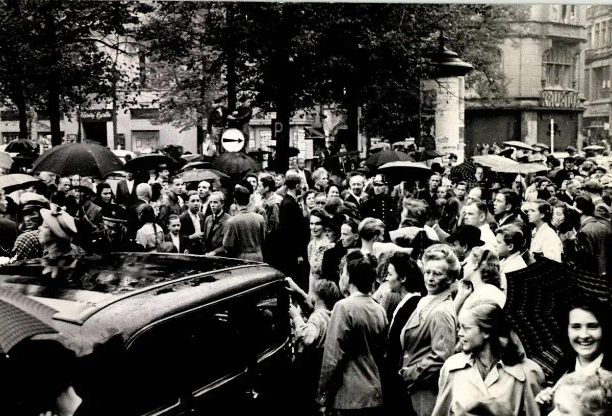 Menschenmenge in Bonn, als die Stadt Hauptstadt war. Ein Auto fährt vor, viele Menschen mit Regenschirmen.