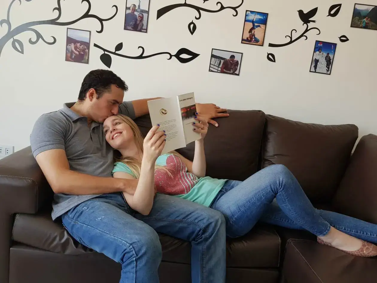 Pareja relajada en un sofá leyendo libros de terapia de pareja. Él le da un beso en la frente.