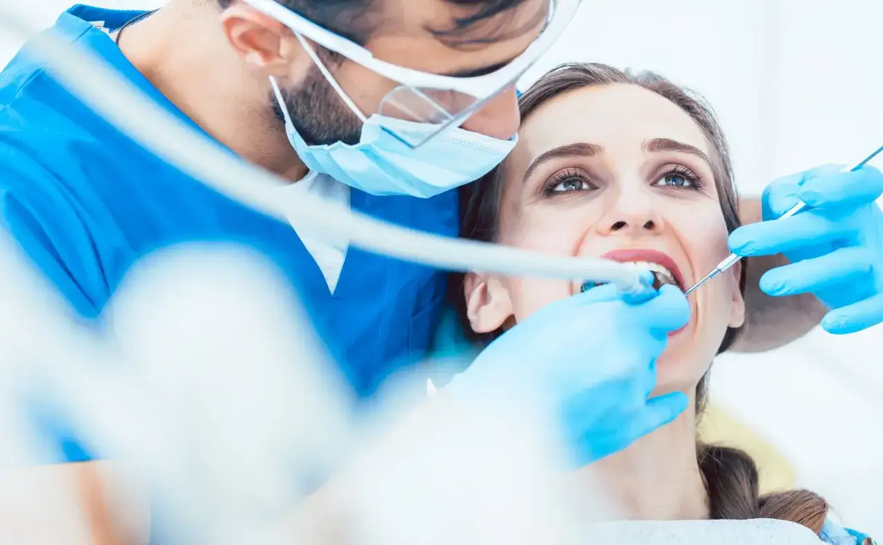 Dentysta w niebieskiej masce i rękawiczkach wykonuje leczenie kanałowe. Sprawdź leczenie kanałowe NFZ cennik.