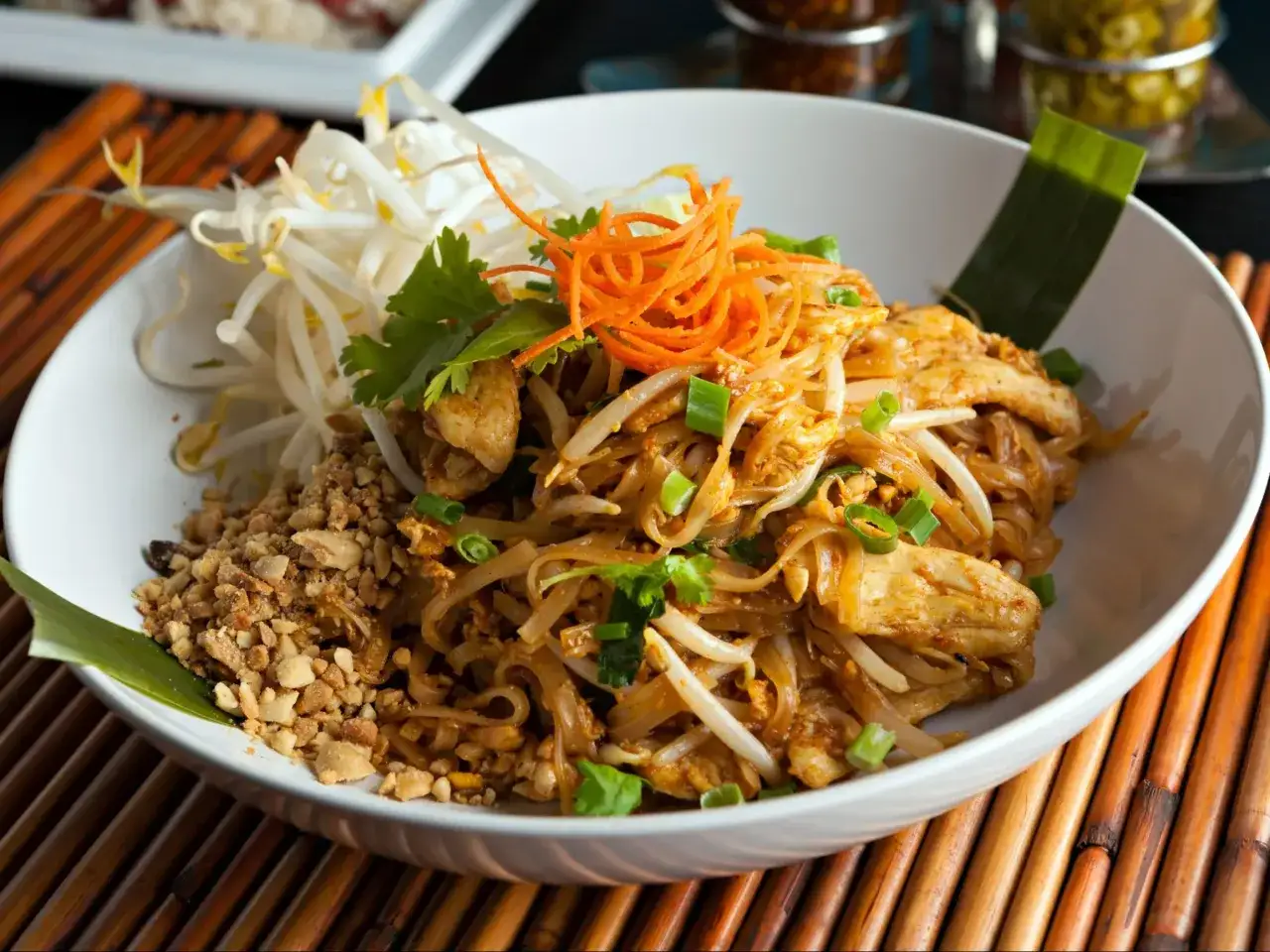 Pyszne pad thai z warzywami, kurczakiem, kiełkami fasoli mung, posypane orzeszkami ziemnymi i posiekanym szczypiorkiem.