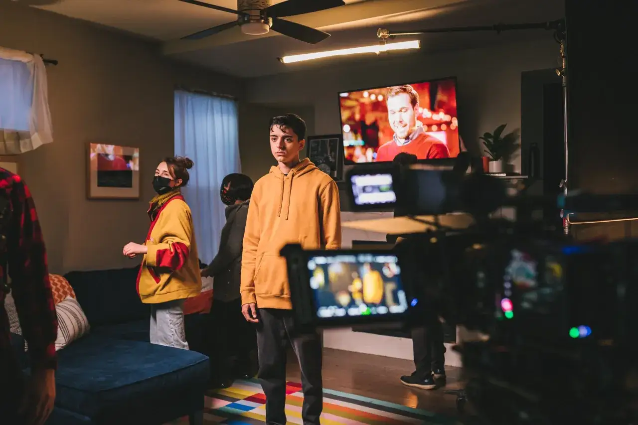 Filming a young man in an orange hoodie, possibly for a social media viral video, with a camera and crew in the foreground.