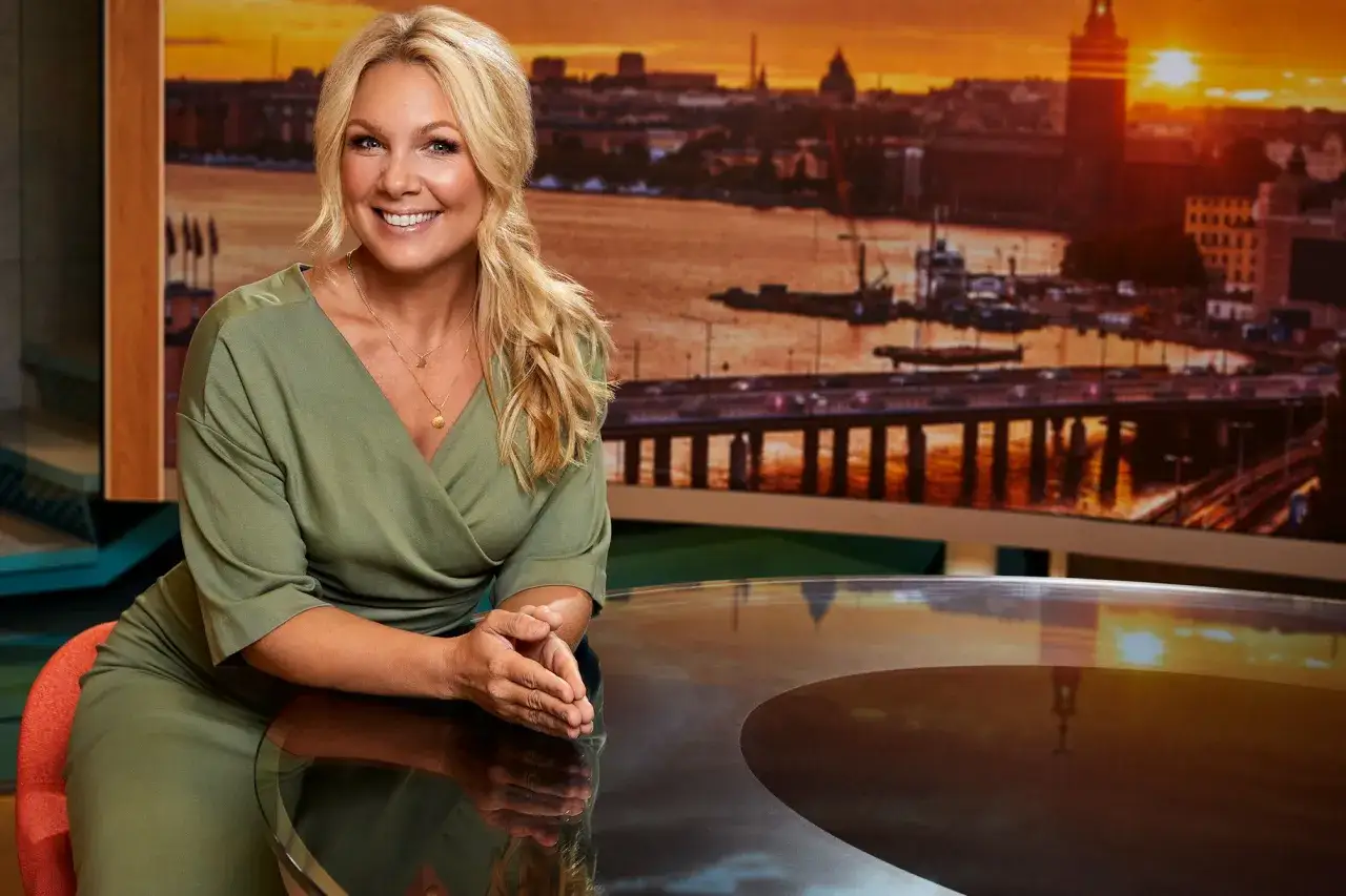 Anna Brolin ler mot kameran i en gr&ouml;n kl&auml;nning, med en bild av Stockholm i solnedg&aring;ngen bakom sig.