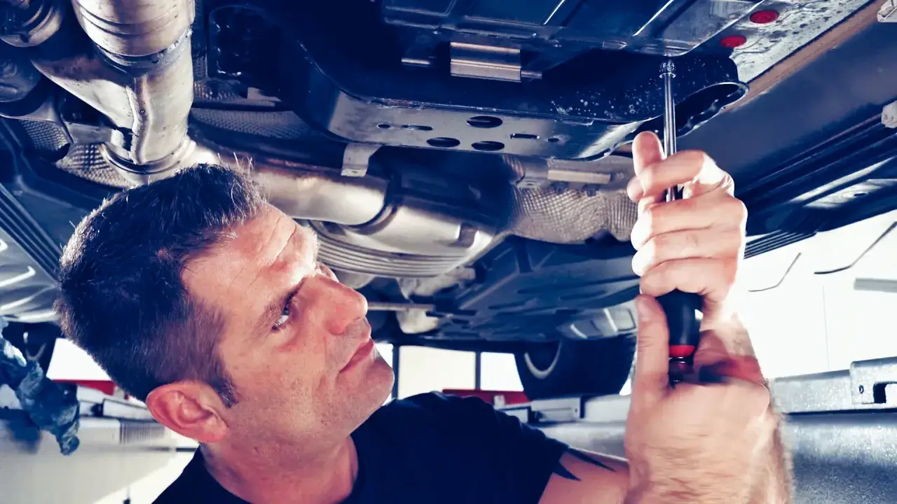 Mechanik pracuje pod samochodem, używając narzędzi do obsługi skrzyni biegów. Płukanka do skrzyni biegów może być częścią tej konserwacji.