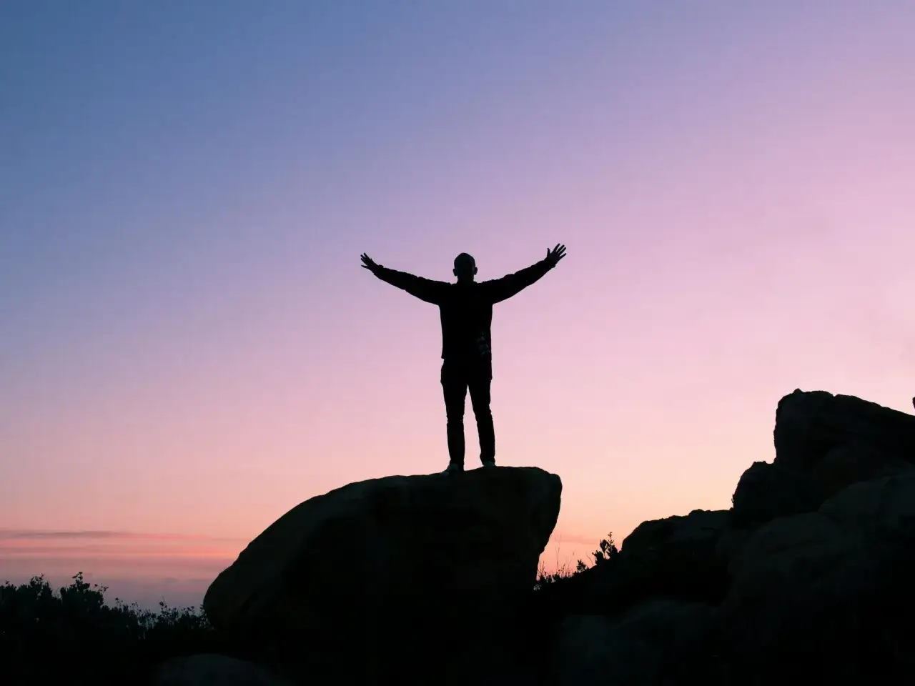 Silhouette of a person with arms outstretched on a rock at sunset. Even though I failed, I still stand tall.