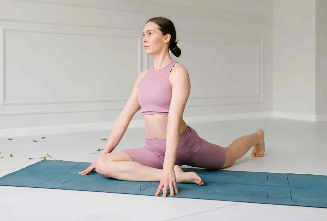 Kobieta w różowym stroju do jogi wykonuje pozycję Eka Pada Rajakapotasana, rozciągając biodro.