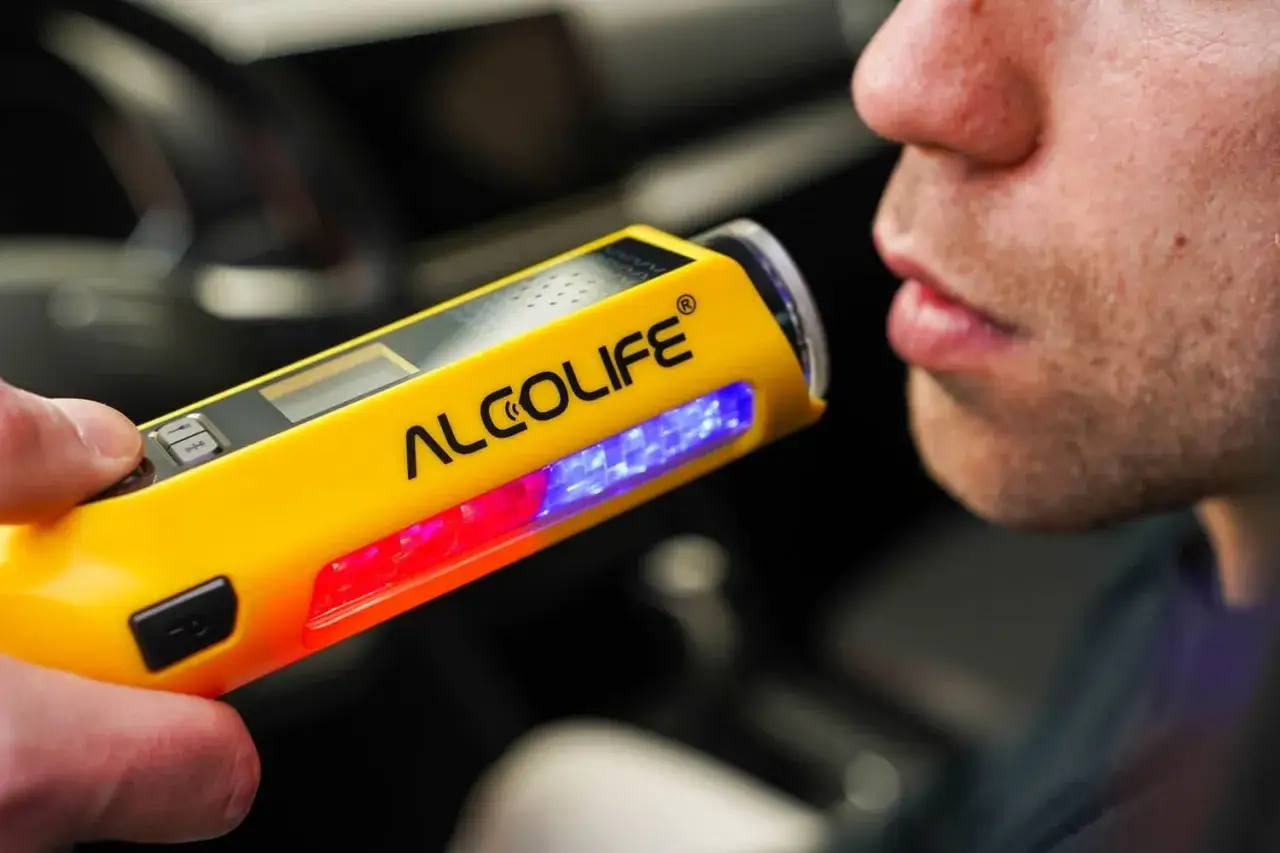 Mężczyzna dmucha w alkomat ALCOSAFE F8. Urządzenie z czerwonym i niebieskim podświetleniem.