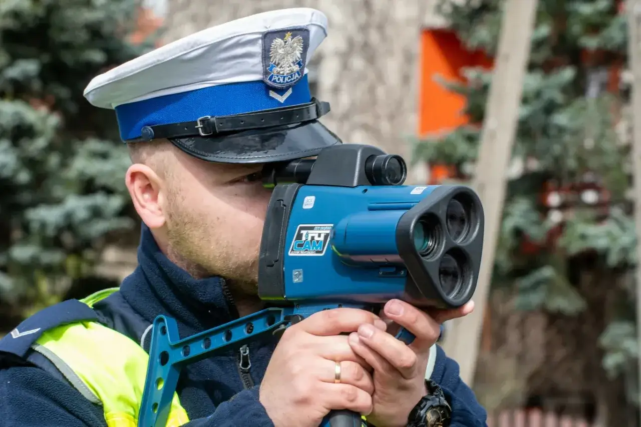 Policjant w czapce z orłem mierzy prędkość. Czy policja może mierzyć prędkość w nocy? Tak, nowoczesne urządzenia pozwalają na to.