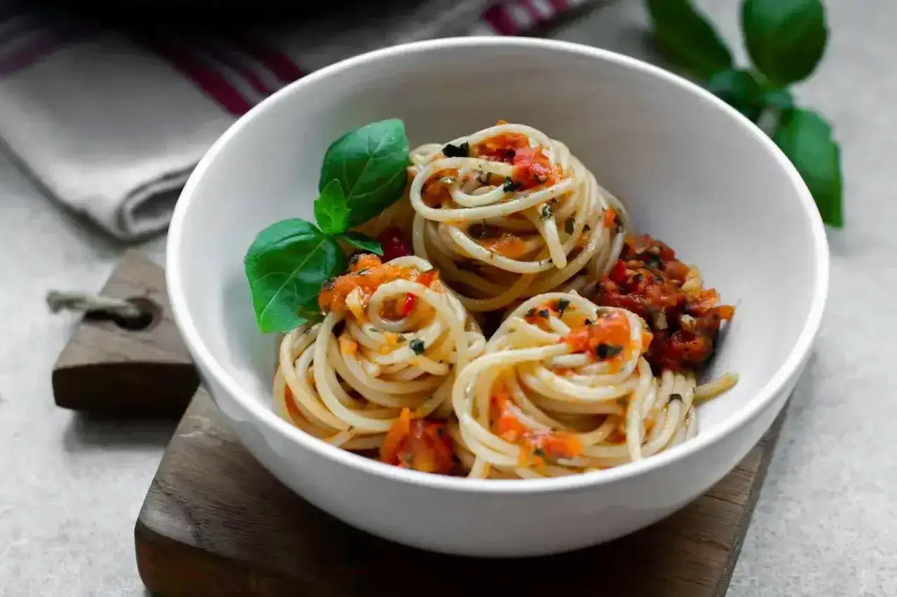 Porcja spaghetti z passatą pomidorową i świeżą bazylią, podana w białej misce na drewnianej desce.