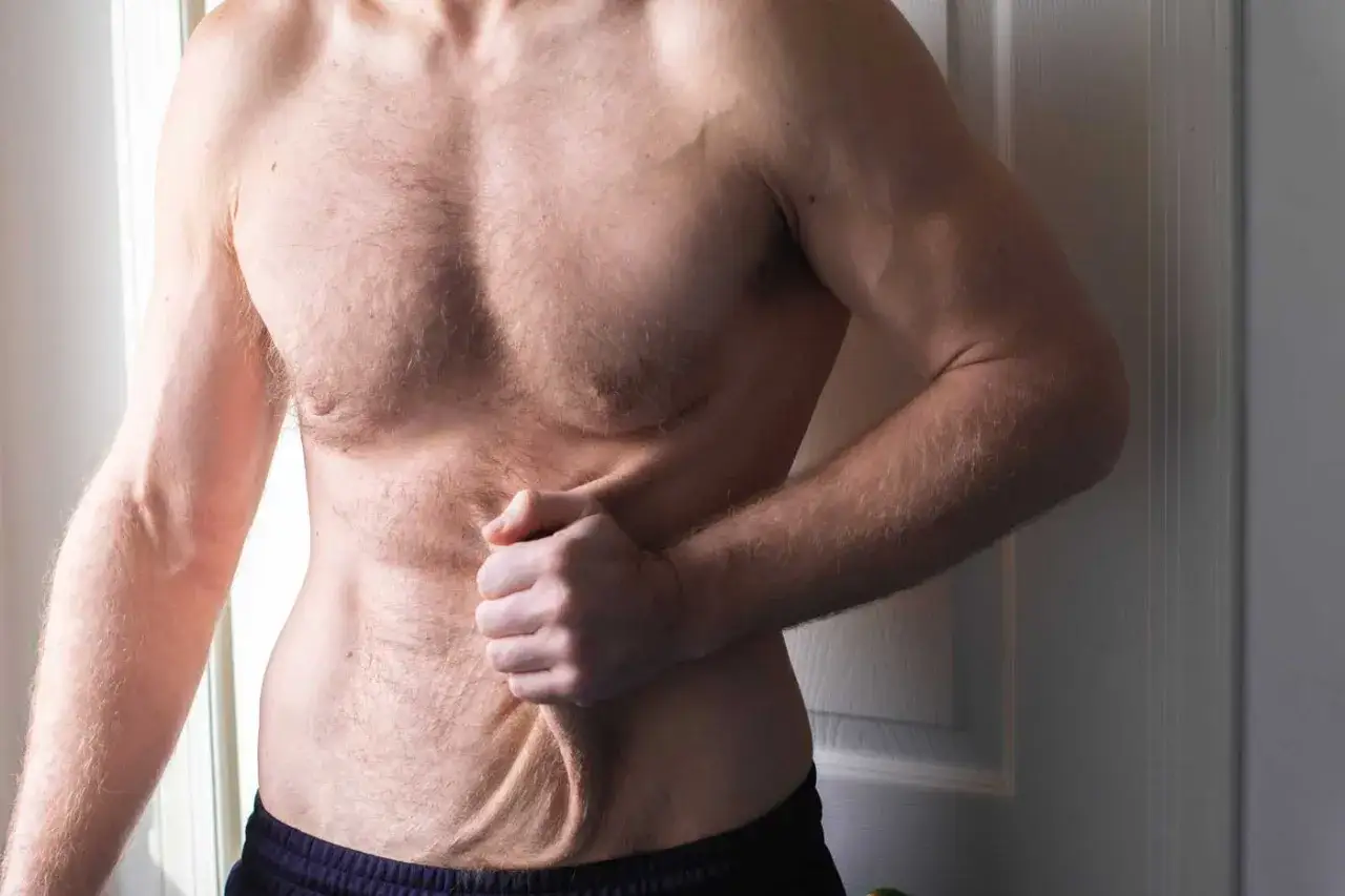 Mężczyzna pokazuje luźną skórę na brzuchu po schudnięciu 40 kg. Widoczne fałdy i nierówności.