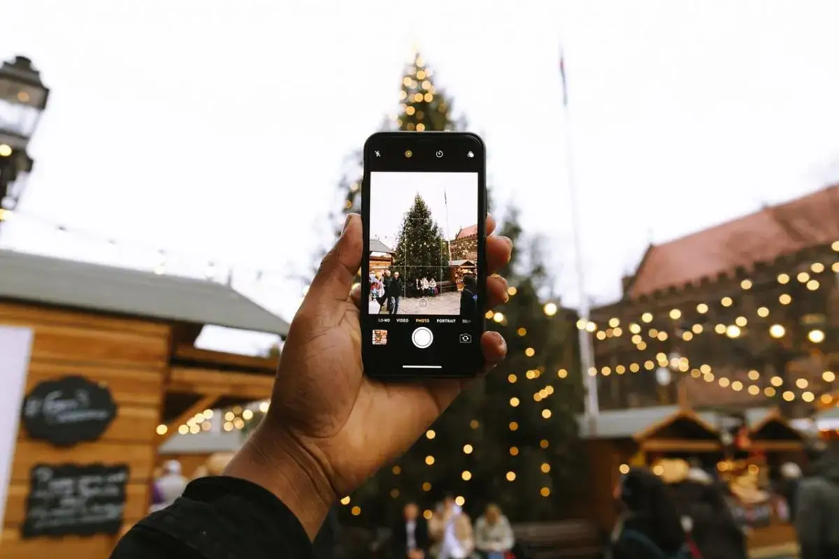 En hand håller upp en mobiltelefon som fotograferar en julgran på en marknad i Alicante i december.
