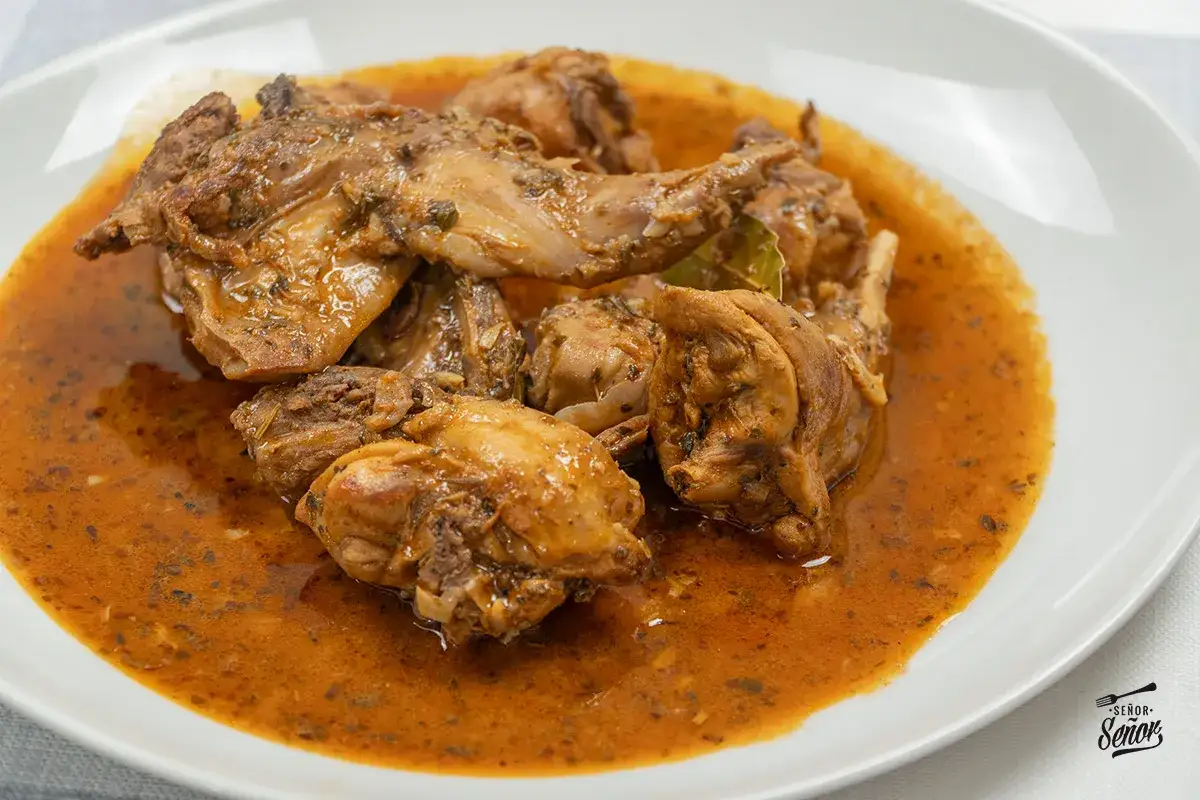 Sabroso conejo en salmorejo, cocinado a fuego lento hasta quedar tierno, servido en un plato blanco.