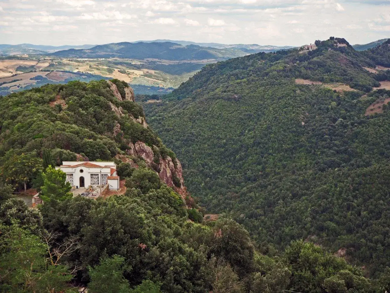 Un edificio bianco su un crinale boscoso nella riserva naturale di Monterufoli-Caselli, con dolci colline sullo sfondo.