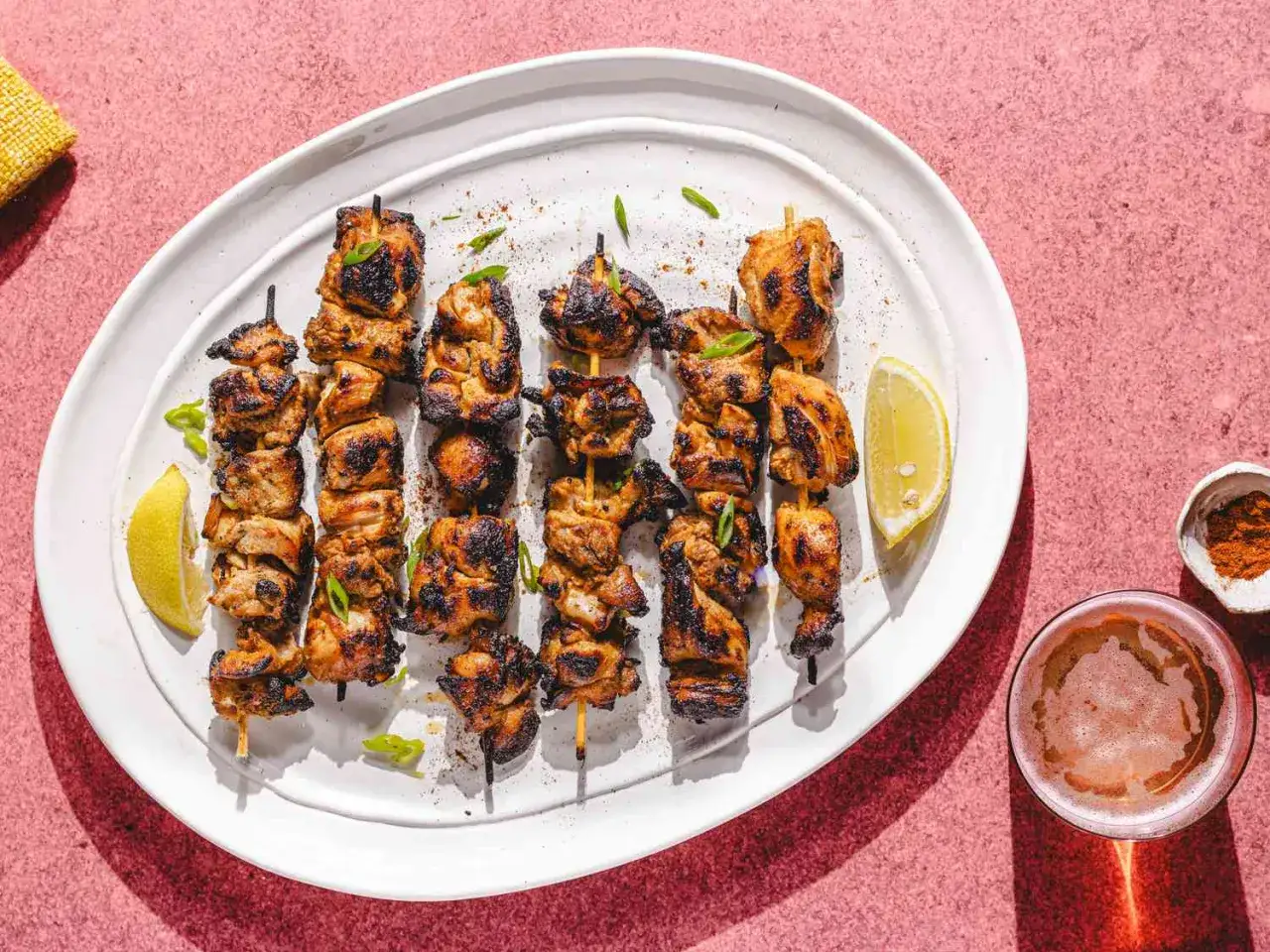 Saftige Chicken Tikka Spie&szlig;e auf einem Teller mit Zitronenspalten und einem Glas Bier.