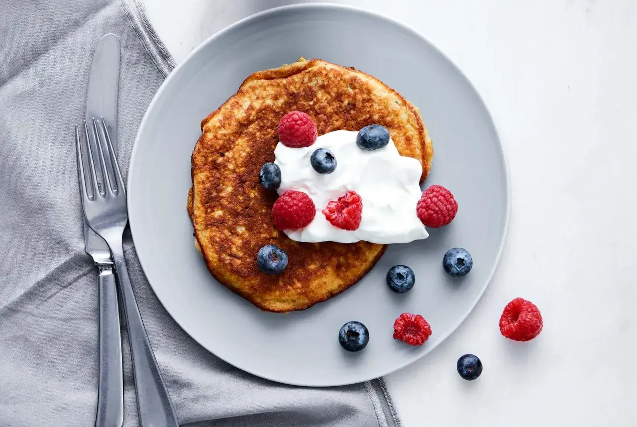 En gyllene bananpannkaka toppad med grädde, blåbär och hallon. Ett perfekt recept på bananpannkaka för en härlig frukost.