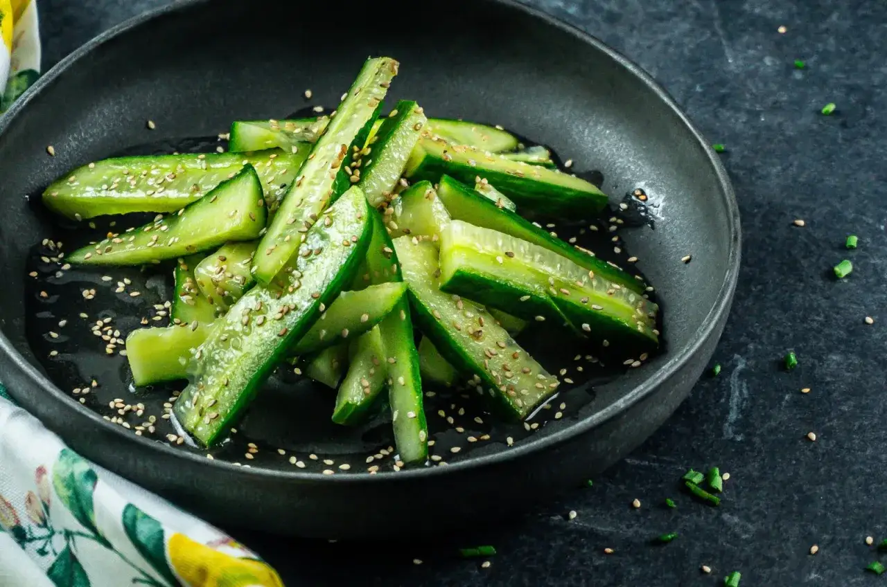 Freshly sliced Japanese cucumber salad, glistening with dressing and sprinkled with sesame seeds, served in a dark bowl.