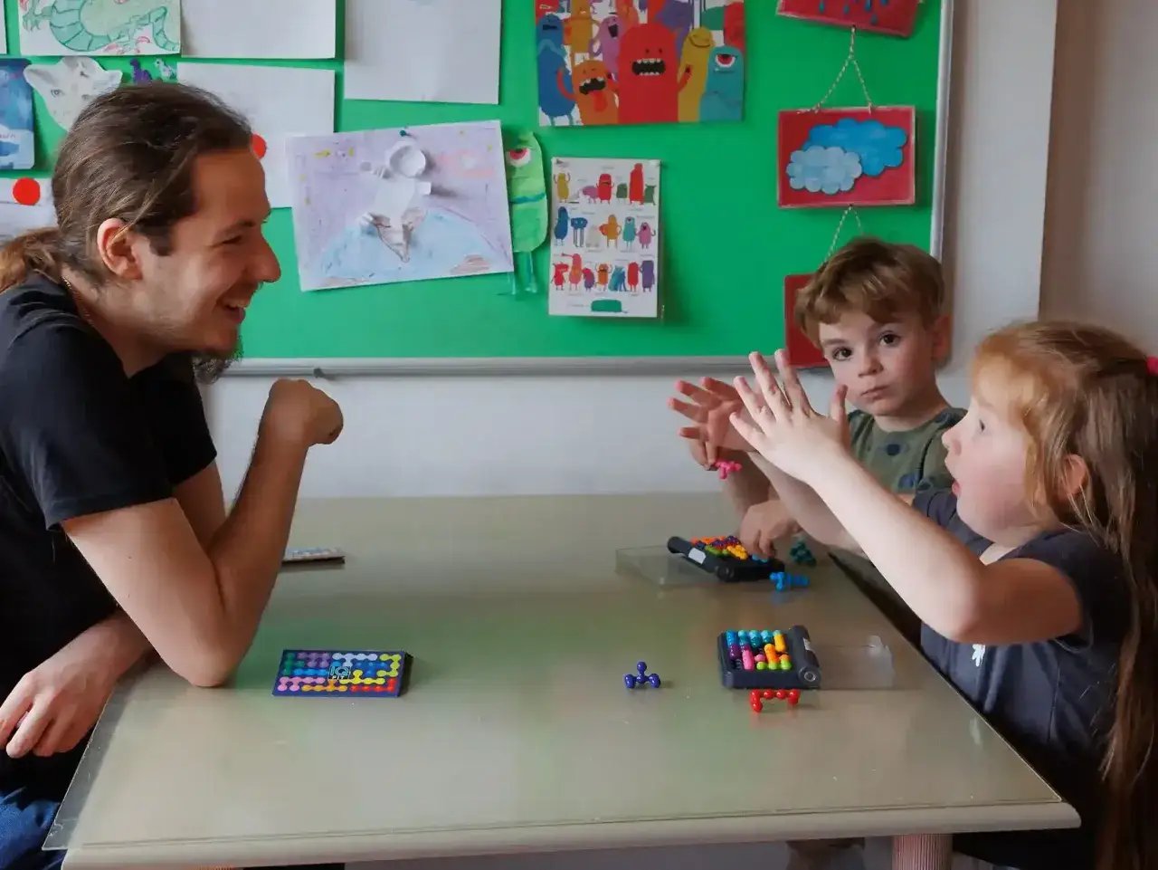 Ein Mann lacht, während er mit zwei Kindern spielt. Sie sind bei der **Ergotherapie für Kinder** und lösen bunte Knobelspiele.
