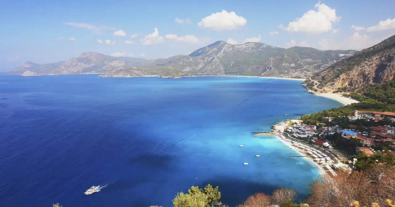 Widok na turkusowe morze i g&oacute;ry w Turcji, Oludeniz. Biała plaża, hotele i ł&oacute;dź na wodzie.