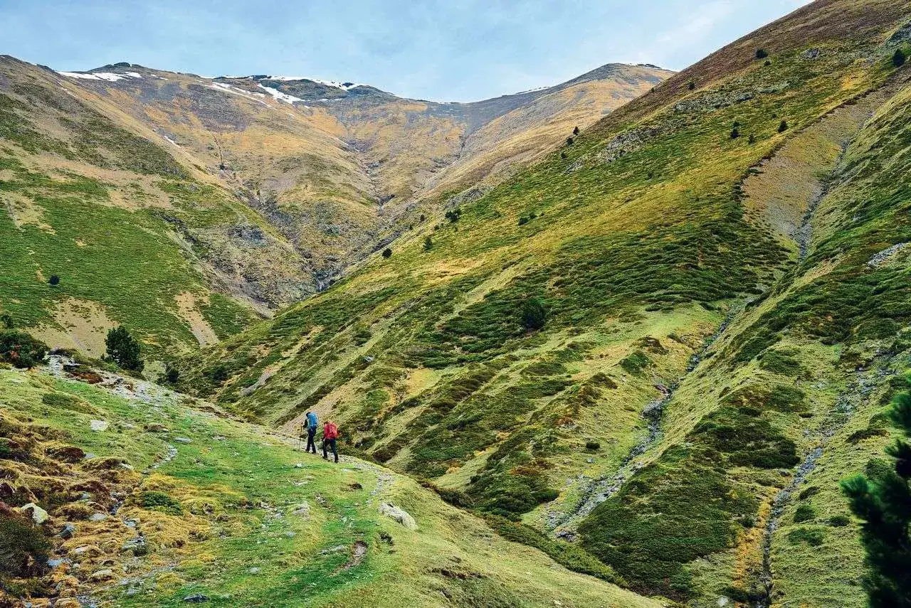 Dos excursionistas caminan por un sendero en un valle montañoso, sintiendo que están en la porta del cel.