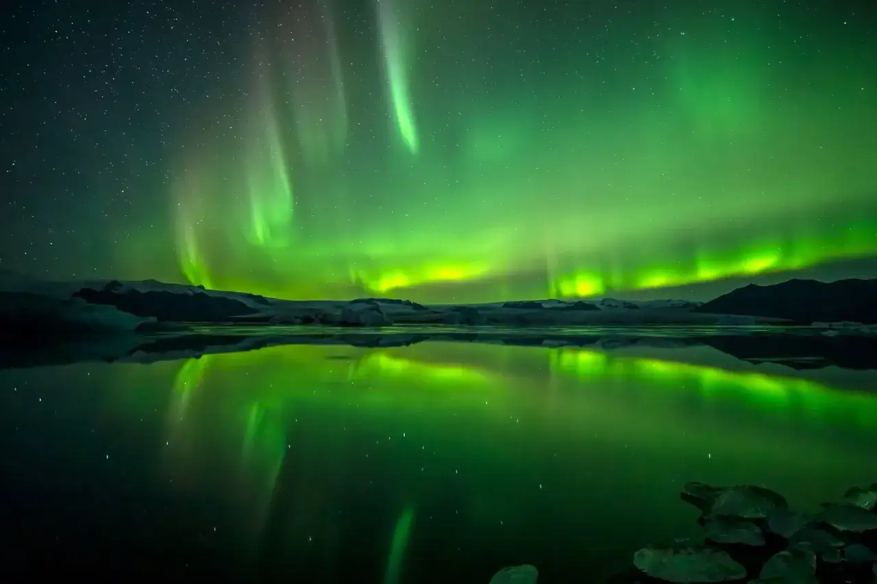 Magnifique ciel étoilé reflété dans l'eau, avec des aurores boréales vertes dansantes. Un guide pour savoir comment photographier les aurores boréales.