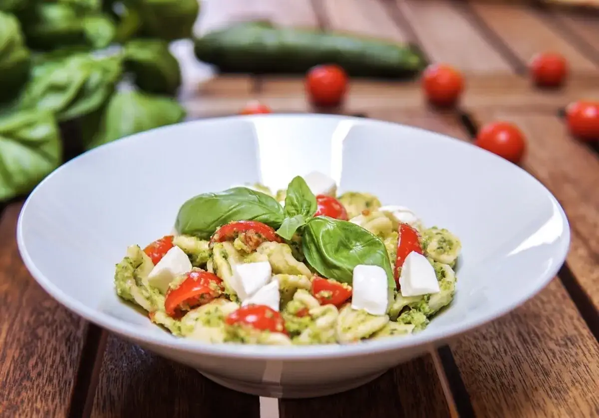 Un piatto di pasta estiva veloce con pesto, pomodorini e mozzarella fresca, guarnito con basilico.