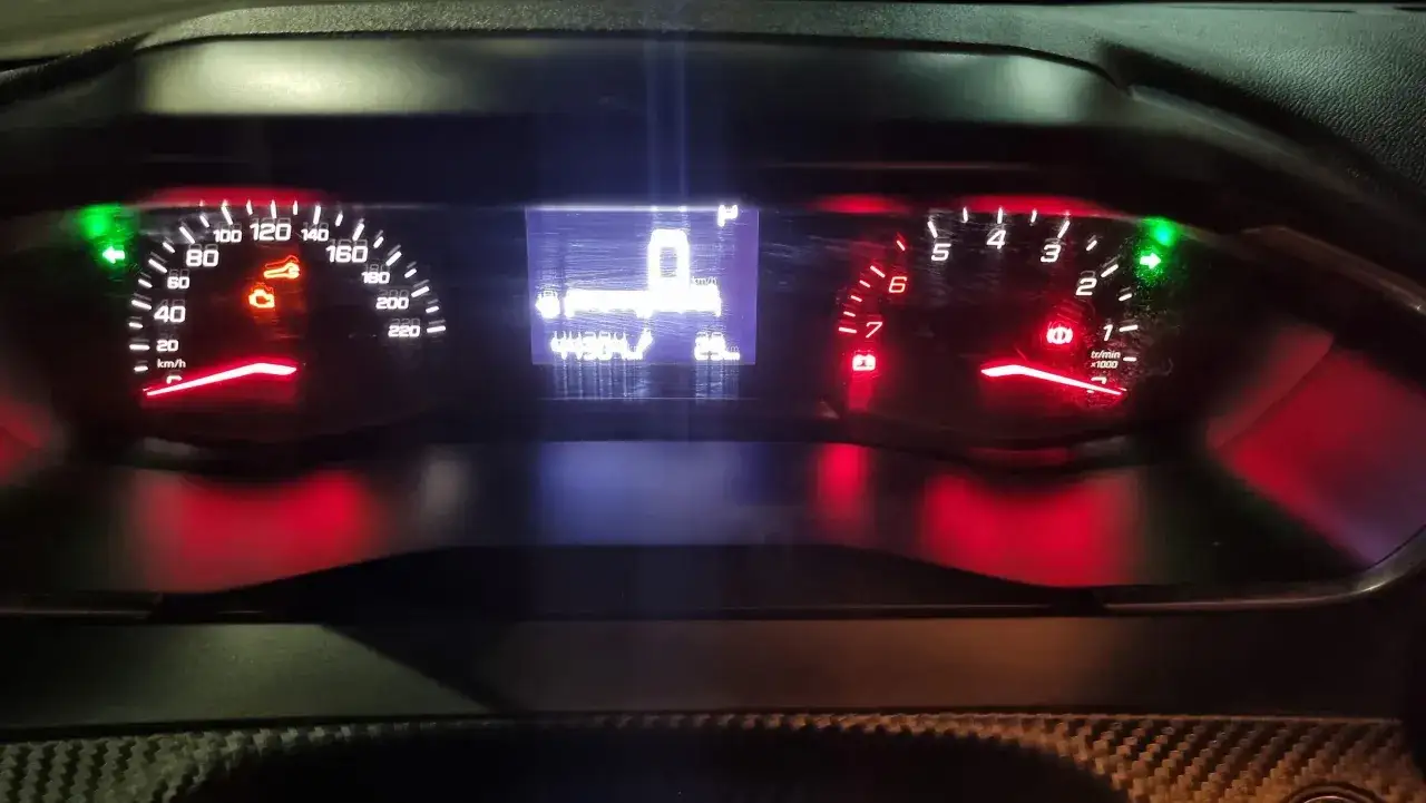 Deska rozdzielcza Peugeot 208 z podświetlonymi wskaźnikami. Widoczny prędkościomierz, obrotomierz i wskaźnik paliwa, sugerujący pojemność baku.