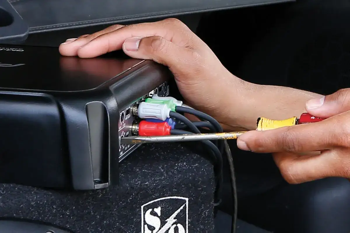 Main d'une personne branchant des câbles RCA sur un amplificateur pour savoir si un caisson de basse fonctionne.