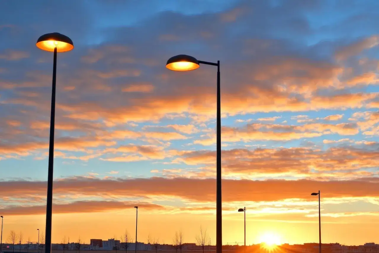 Deux lampadaires s'allument sous un ciel aux couleurs flamboyantes, annon&ccedil;ant le coucher du soleil.