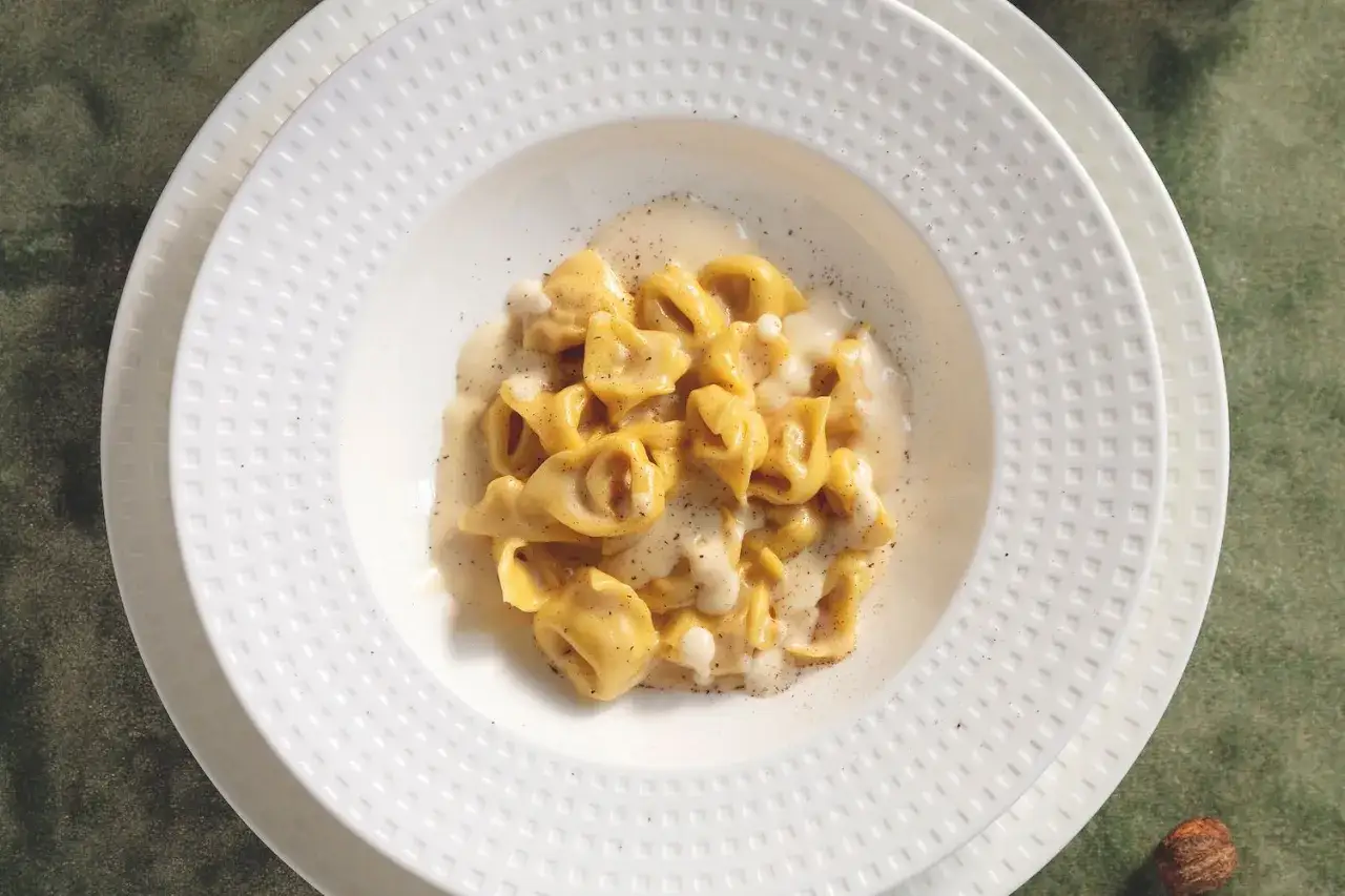Tortellini freschi immersi in una cremosa fonduta di parmigiano, guarniti con pepe nero macinato. Un piatto che sa di casa.