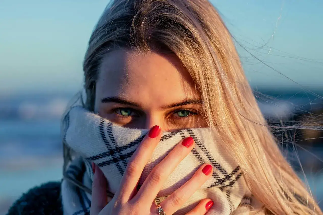 Dziewczyna z zielonymi oczami, częściowo zakryta wzorzystą chustą buff. Wiatr rozwiewa jej blond włosy.