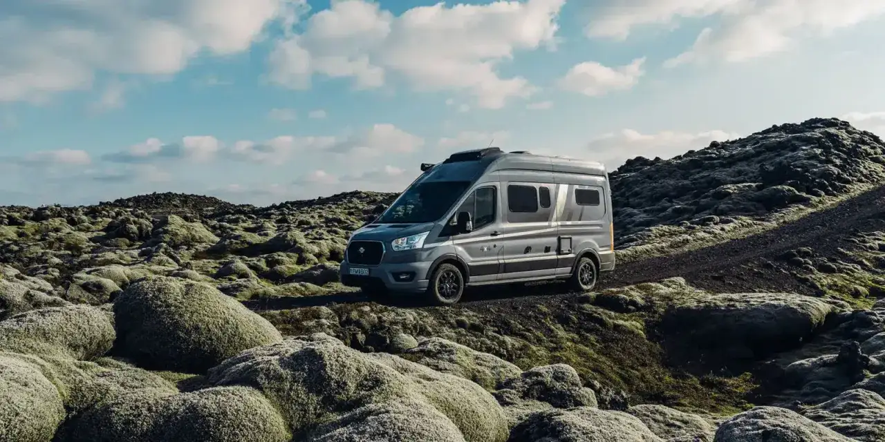 Grauer Campervan auf felsiger, moosbewachsener Landschaft. Perfekt für Island Wildcampen unter blauem Himmel mit Wolken.