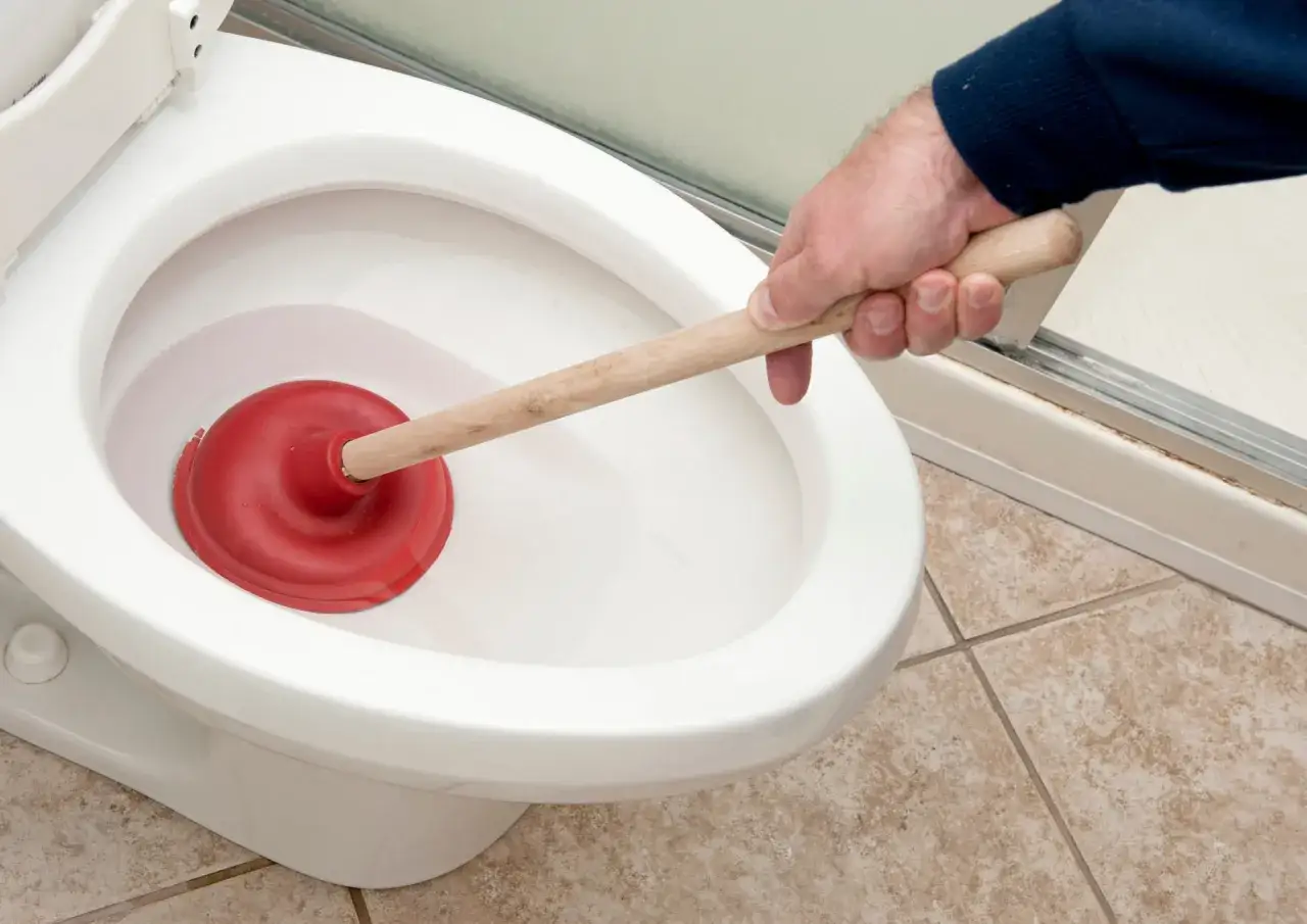 Main d'homme utilisant une ventouse rouge pour déboucher un WC.